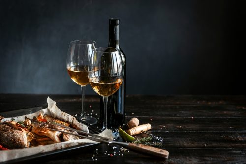Wine bottle with two partially filled wine glasses on a dark wooden table, surrounded by torn bread and breadcrumbs in the foreground.