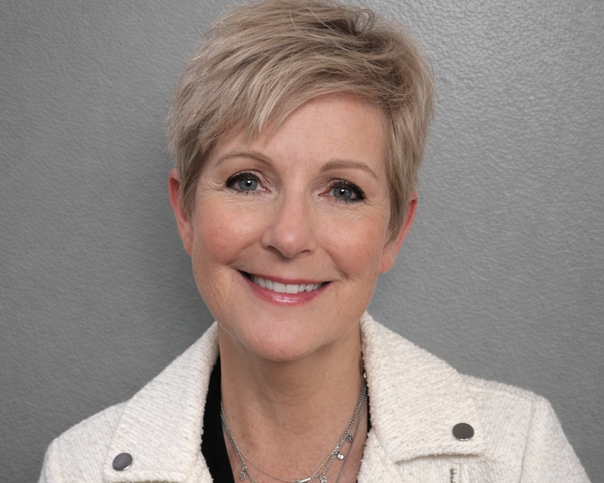 Smiling woman with short blonde hair wearing a white textured jacket, against a gray background (headshot).