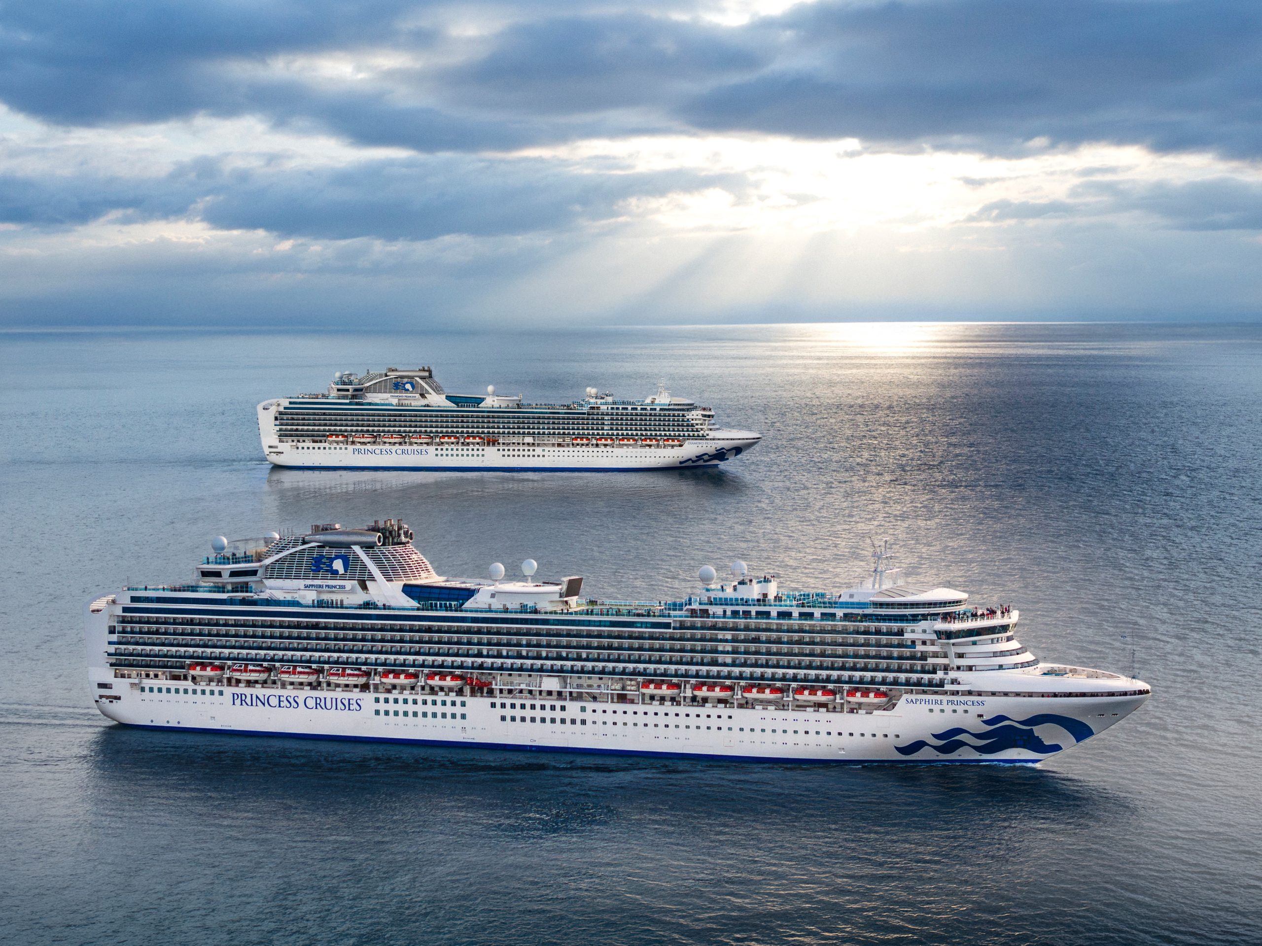 Two large Princess Cruises ships sail on calm blue water under a cloudy sky, with the word PRINCESS CRUISES visible on the hull of the foreground vessel.