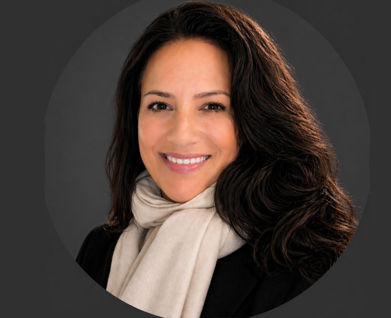 Laura McDonald Headshot Landscape | Holiday Planit Professional headshot of a smiling woman with long dark hair, wearing a beige scarf and black coat against a dark gray backdrop.