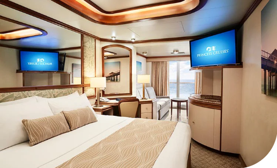 Elegant cruise cabin with a large bed, warm wood accents, and twin TVs displaying Princess Cruises in-room content.