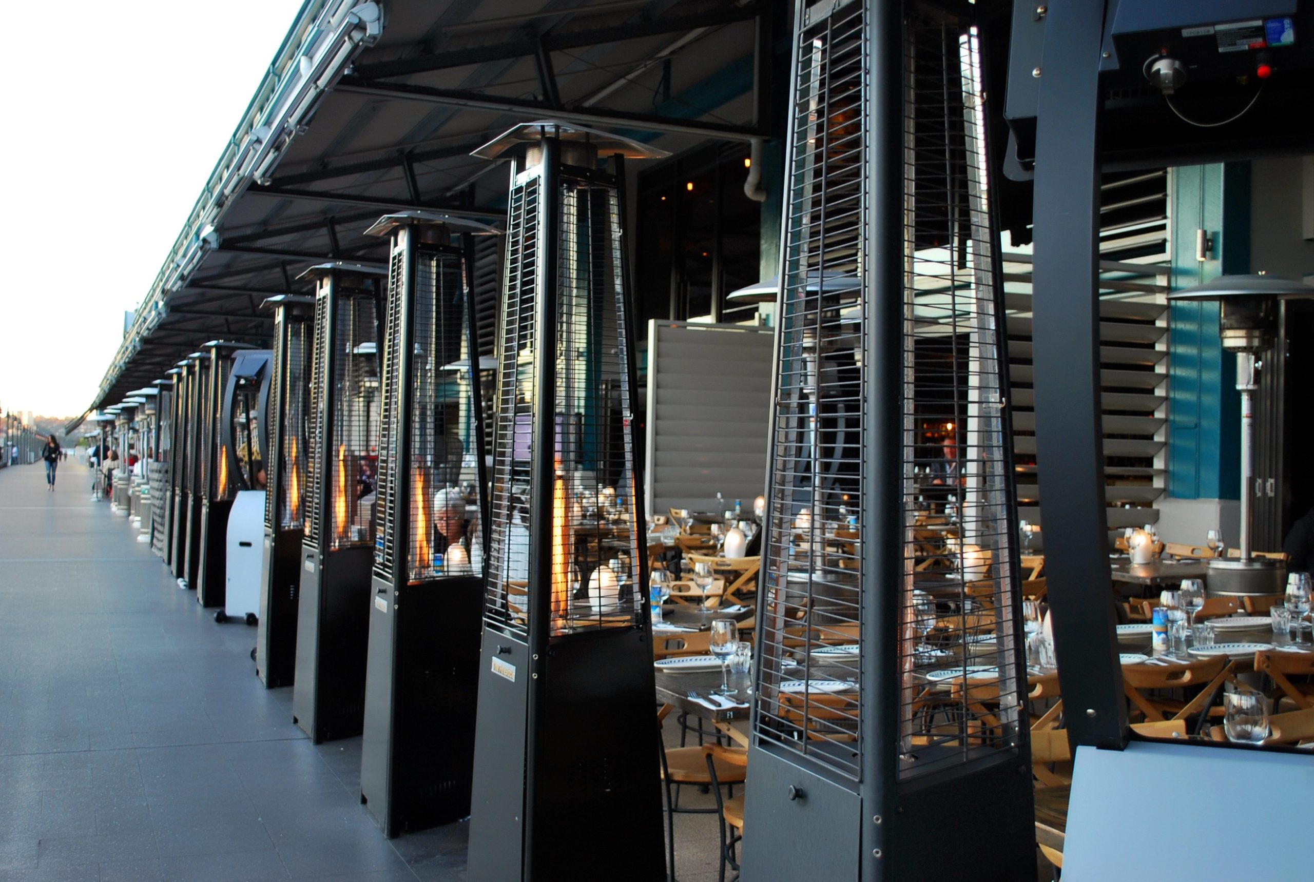 Woolloomooloo wharf luxury dining area | Holiday Planit Row of tall outdoor patio heaters beside a covered restaurant dining area with tables set for guests.