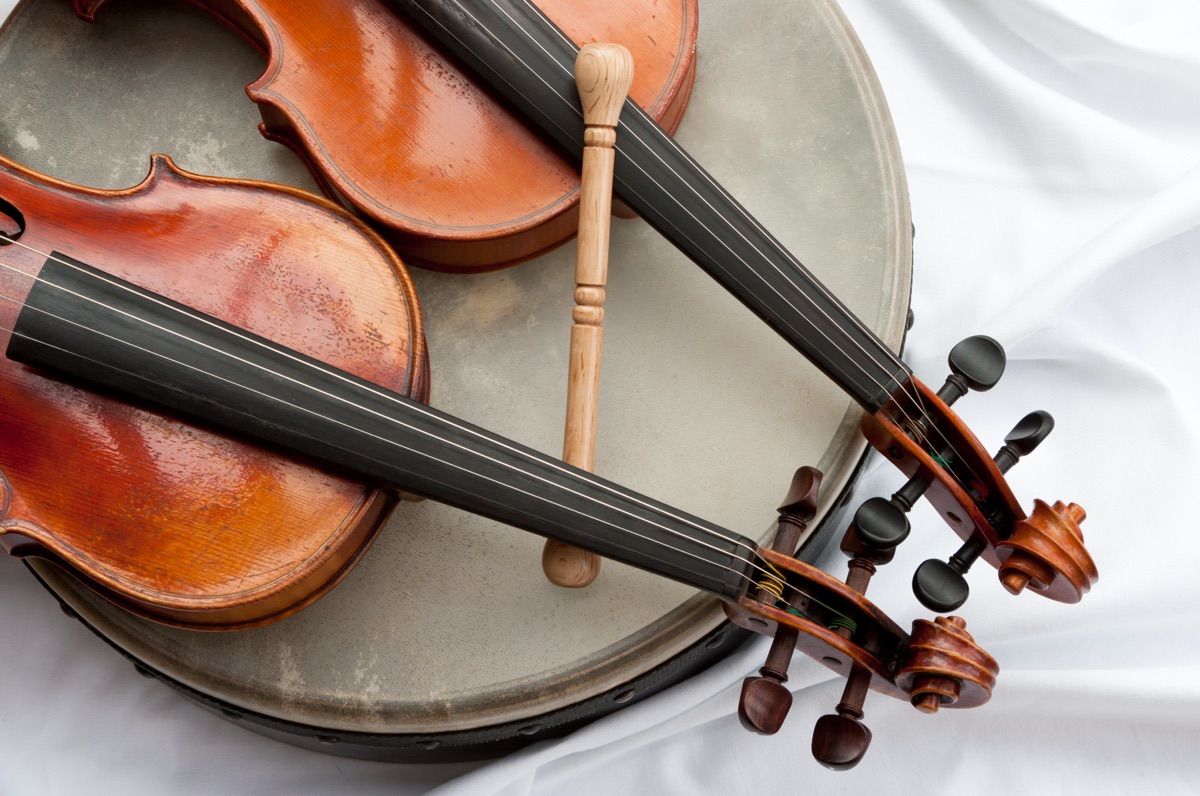 Irish folk 2 Geigen mit Bodhran | Holiday Planit Two violins with bows resting across a round drum, shown in a close-up view on white fabric.