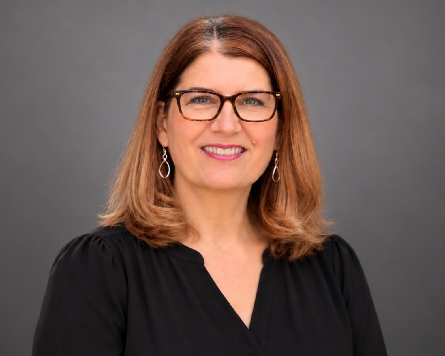 Smiling woman with wearing a black shirt against a gray studio backdrop (professional headshot).